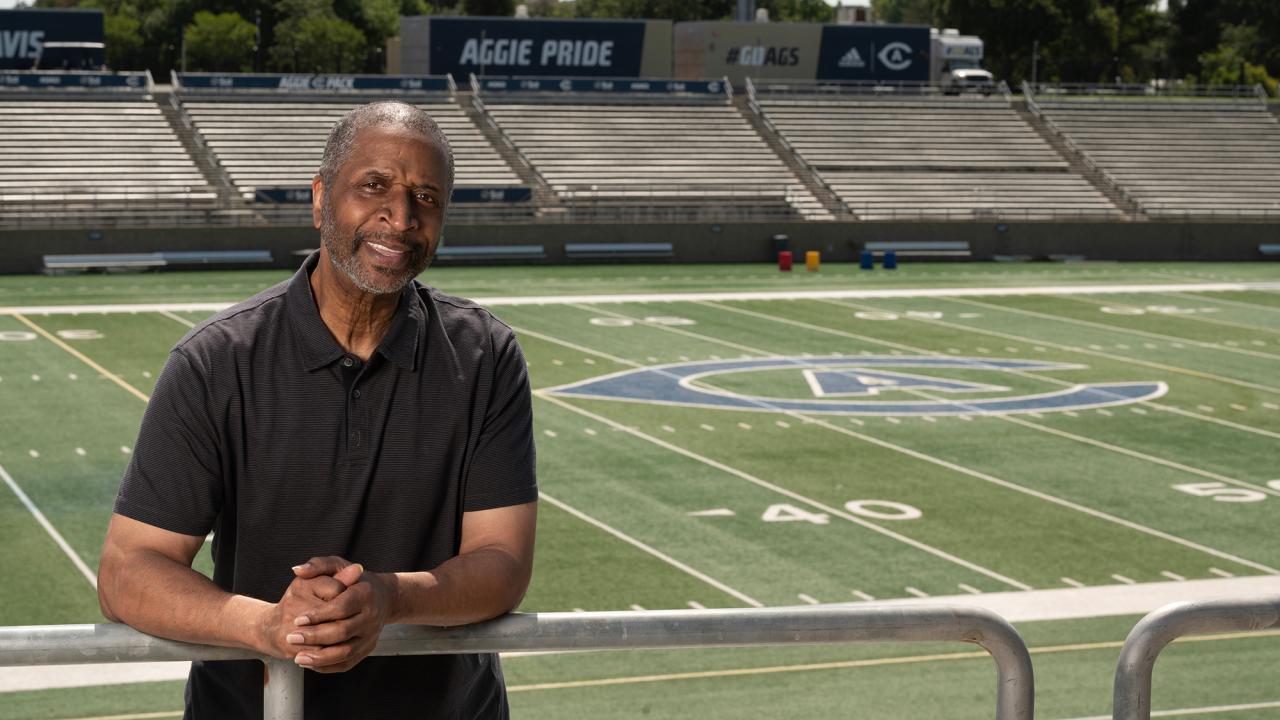 With the football field in the background, Ron Austin leans against the top rail of seating at UC Davis Health Stadium