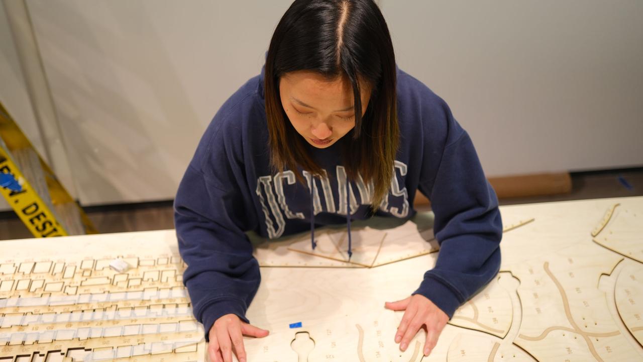 Student with long dark hair and sweatshirt works on plans