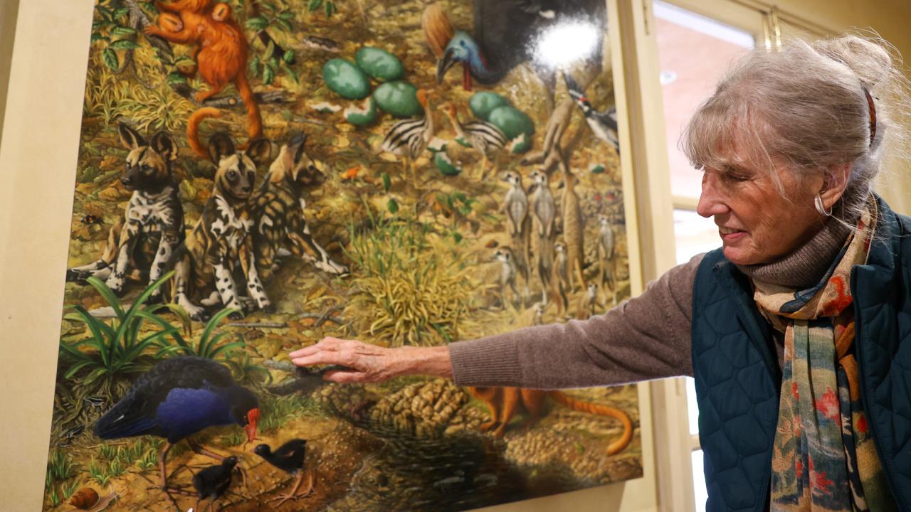 A woman shows a large painting of several animals