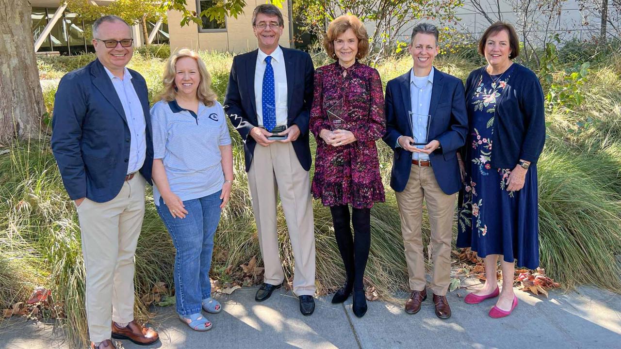 Six people pose for photo. Three of them hold awards.