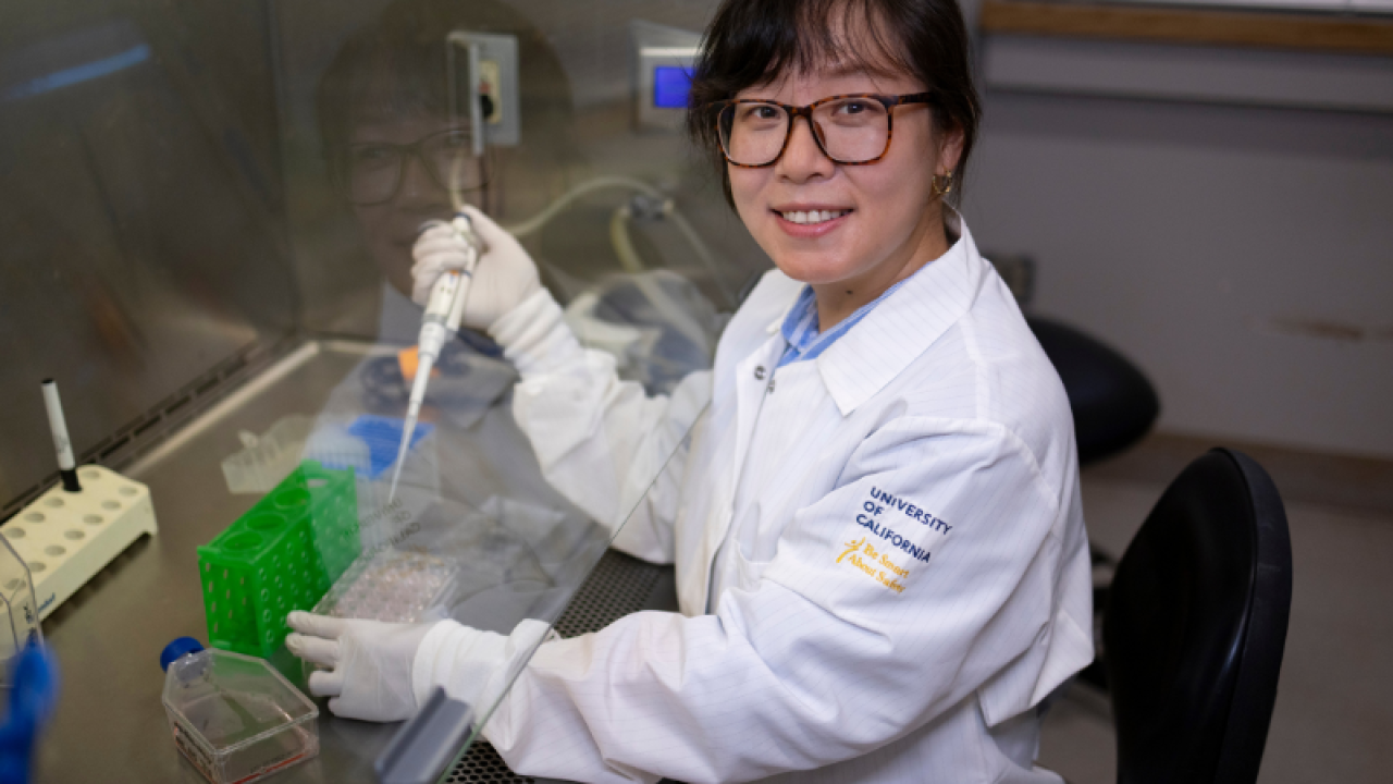 A woman wearing a University of California lab coat works with samples in a laboratory environment