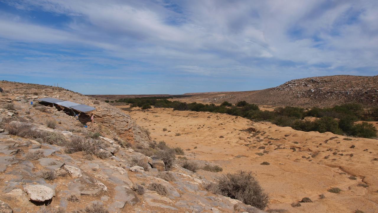 Arid landscape with shade cover over archaeological dig to left hand side. 