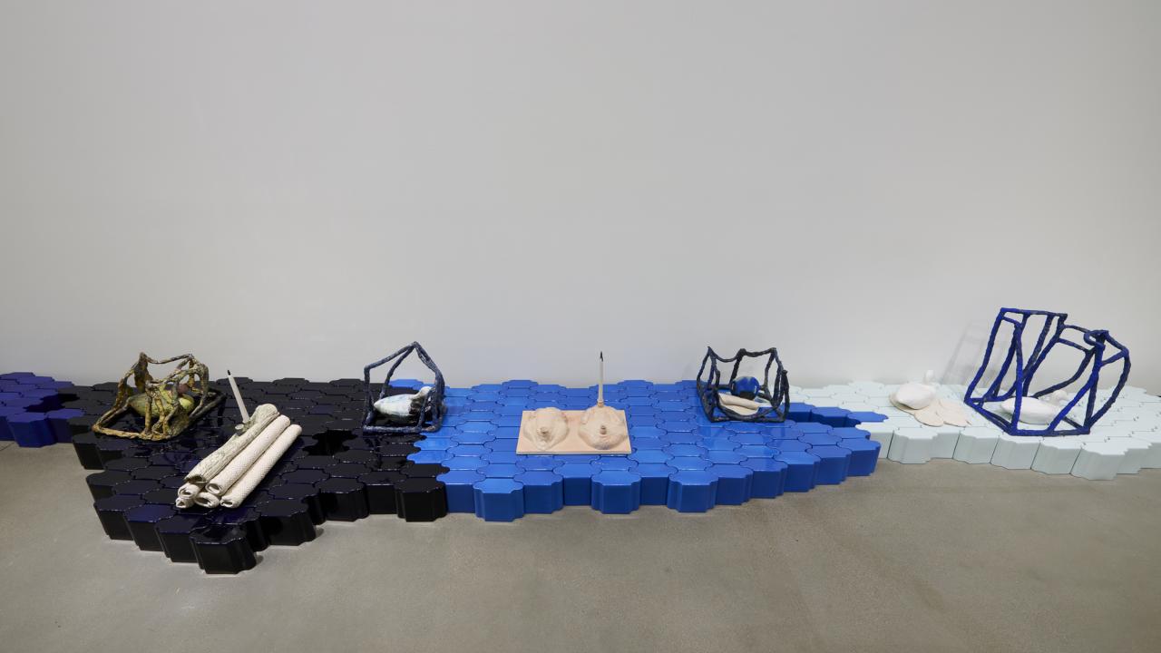 An abstract art installation featuring blue, black, and white forms arranged on the floor. with tile, duck decoys and other forms.