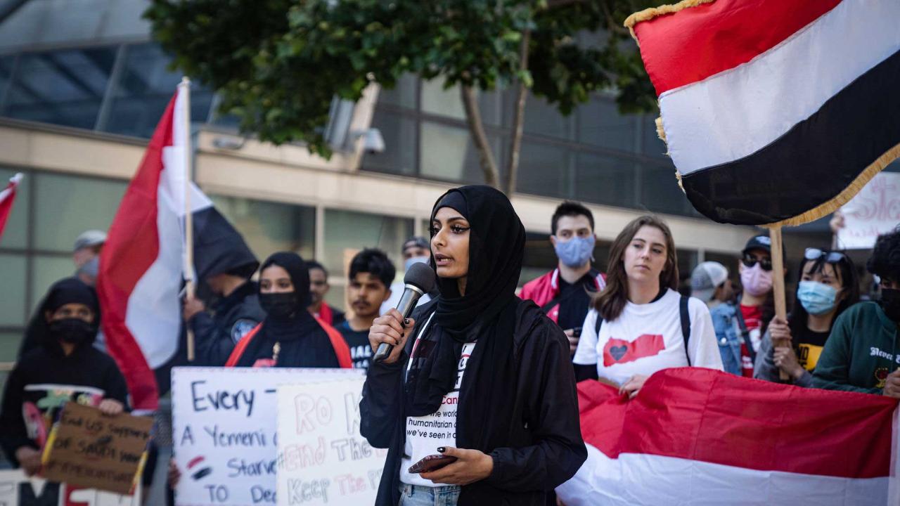 Woman at protest. Colorful flags surround her.