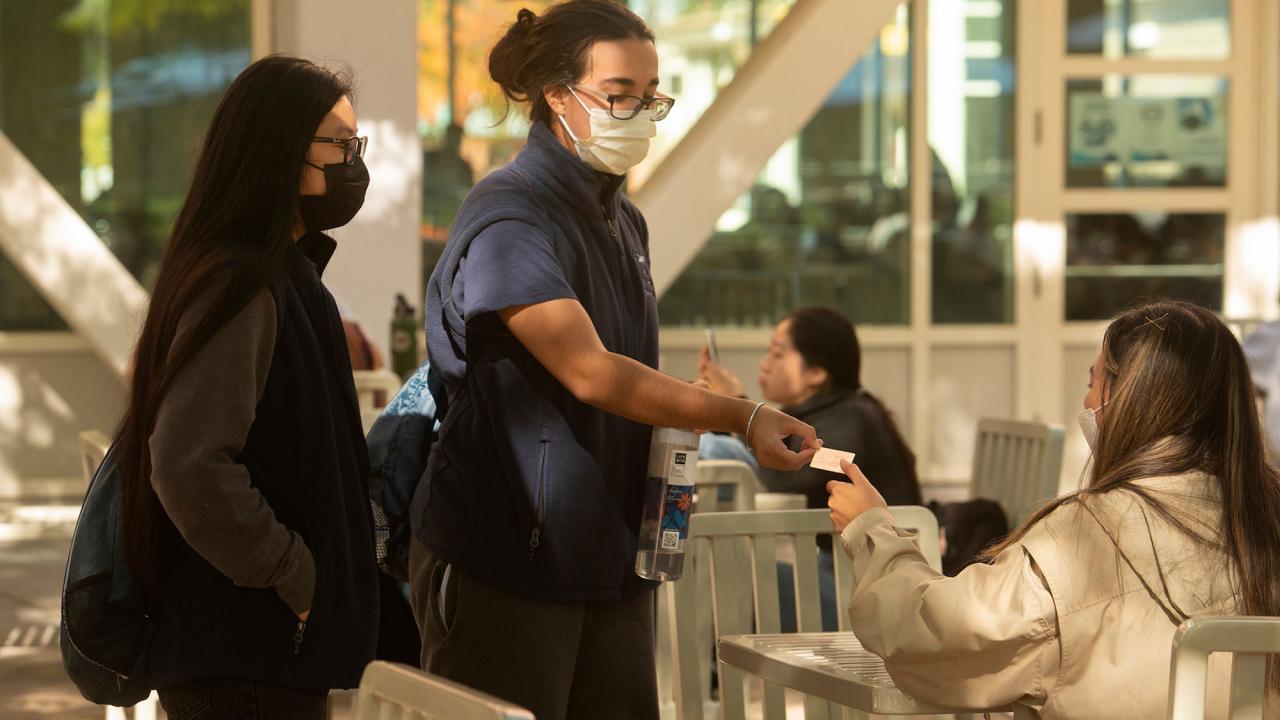 Two standing students give gift card to sitting student.