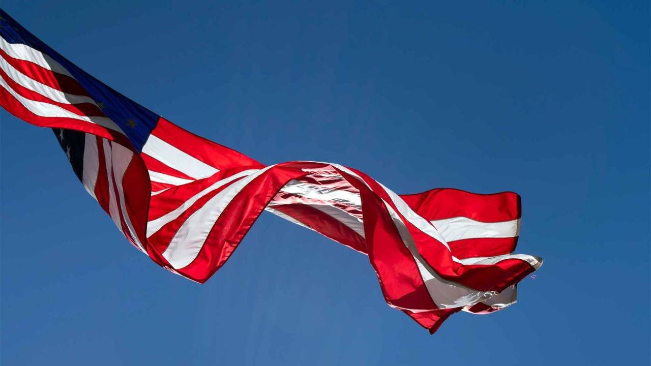 An American flag waves in the wind against a blue sky.