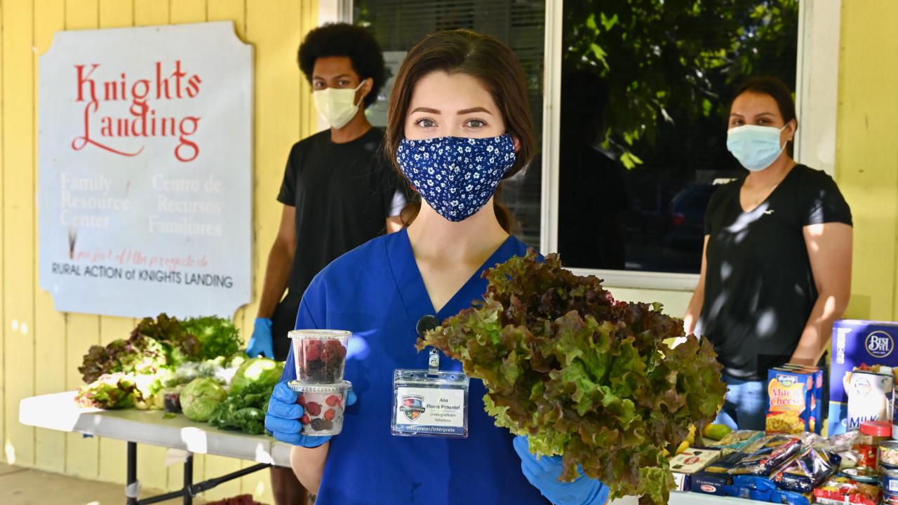 Woman in mask holds snacks and produce.