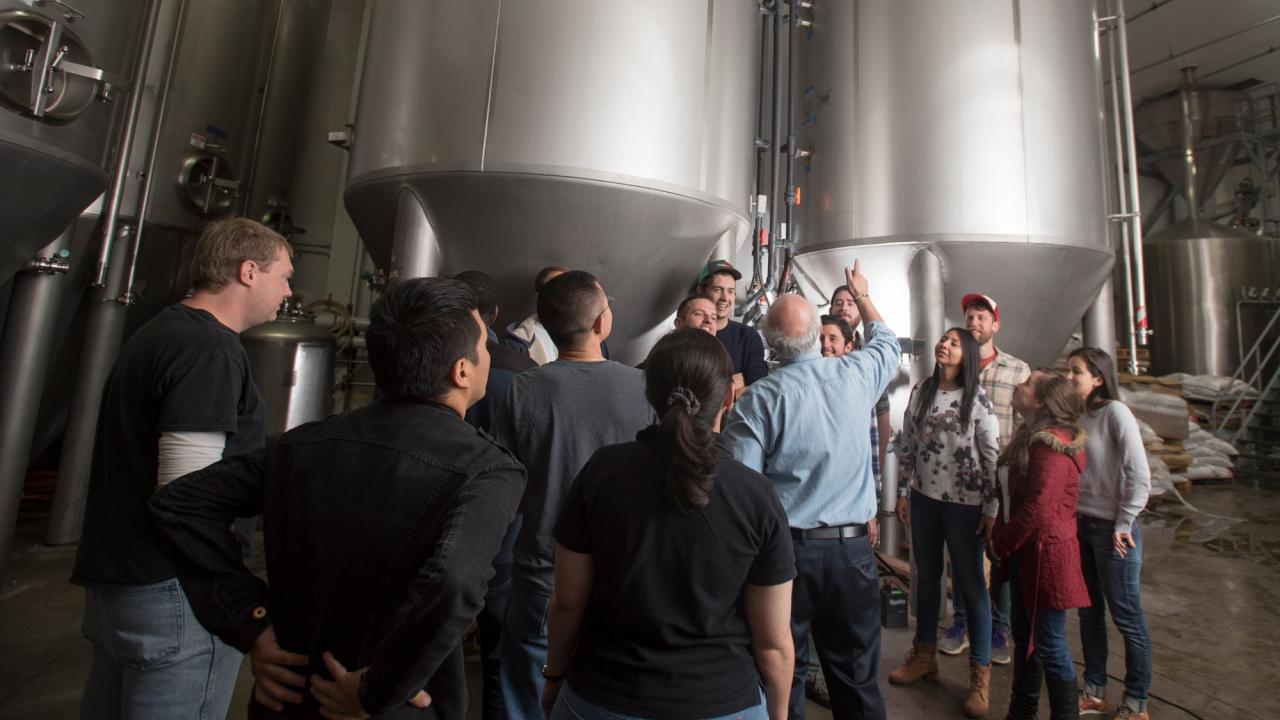 Class gathers around brewing equipment (two giant tanks).
