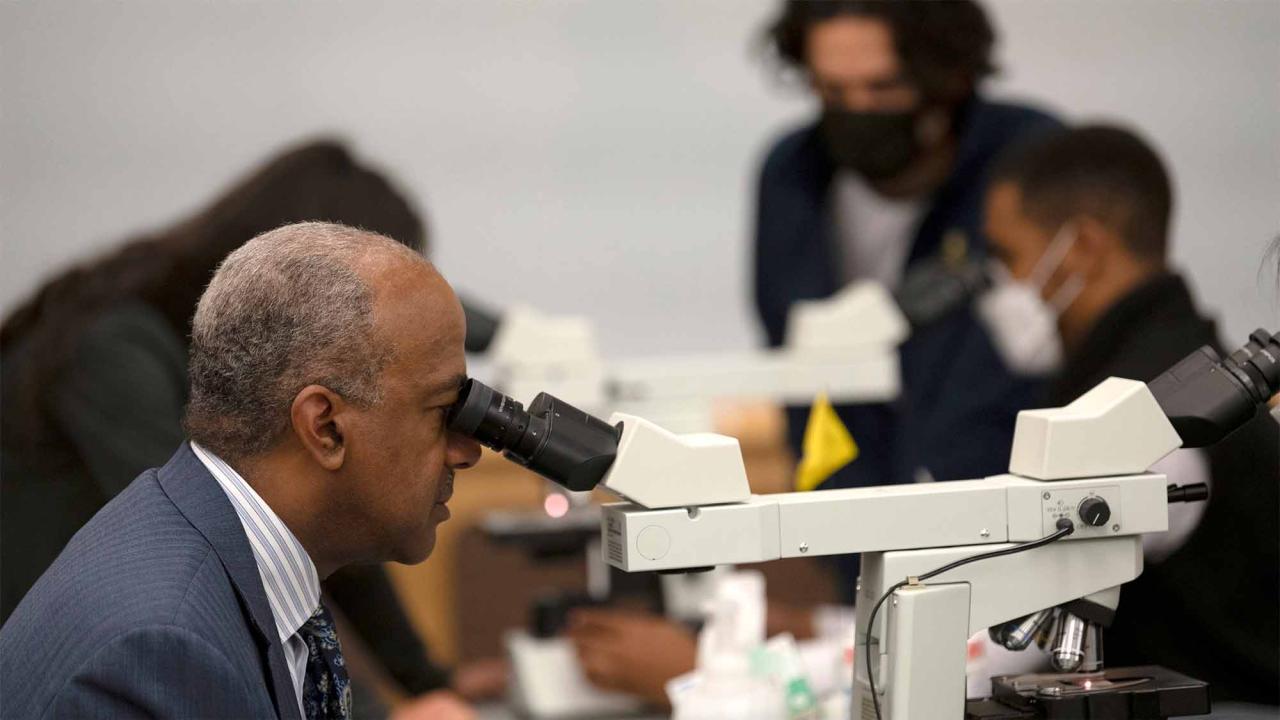 Chancellor Gary S. May looks into a microscope.