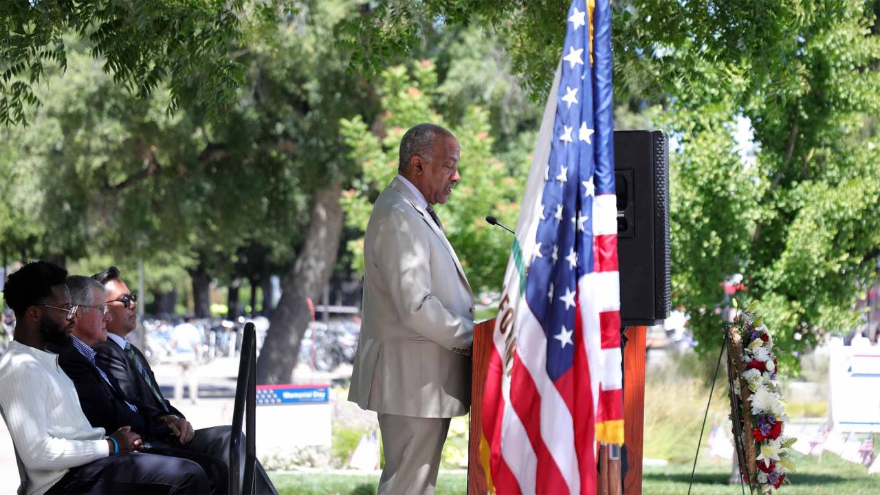 Chancellor Gary S. May speaks on stage next to American flag