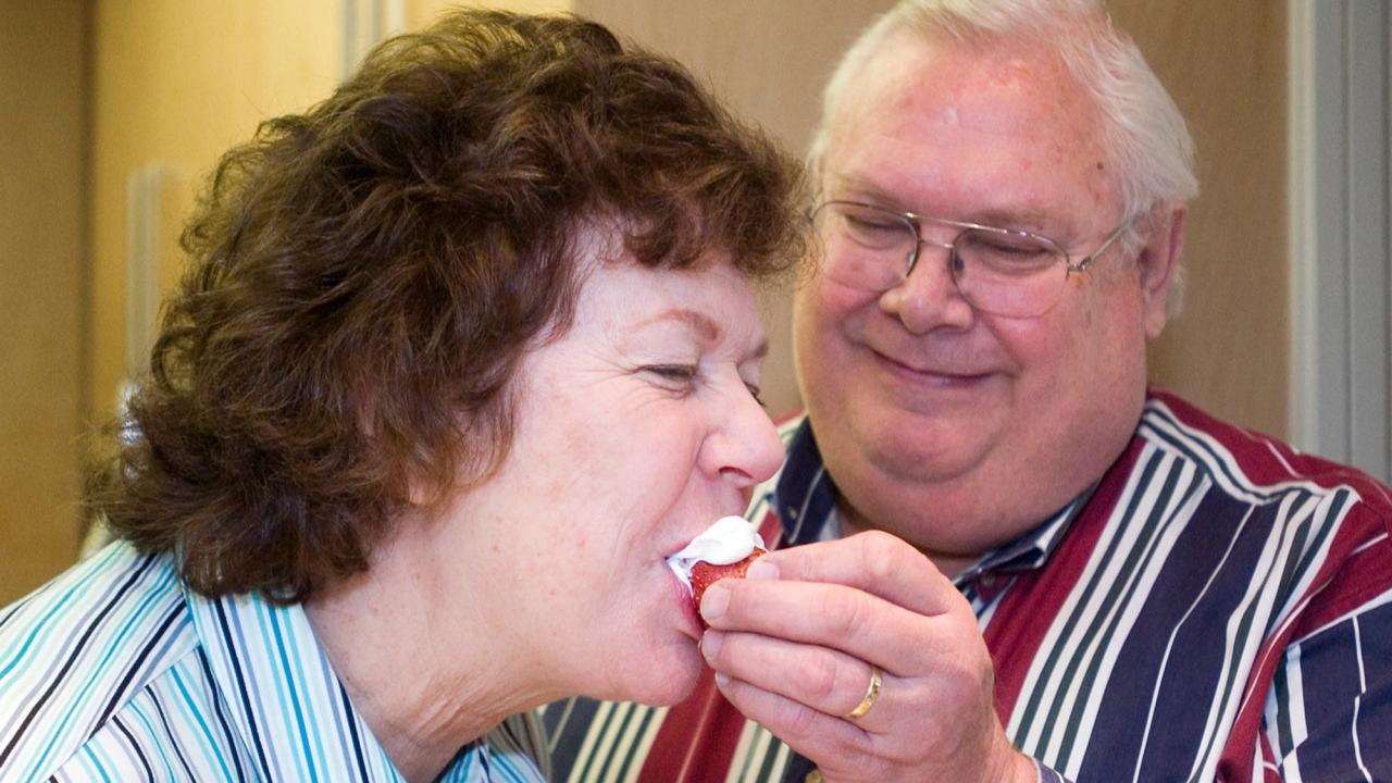 Man feeds strawberry dipped in whipped cream, to woman