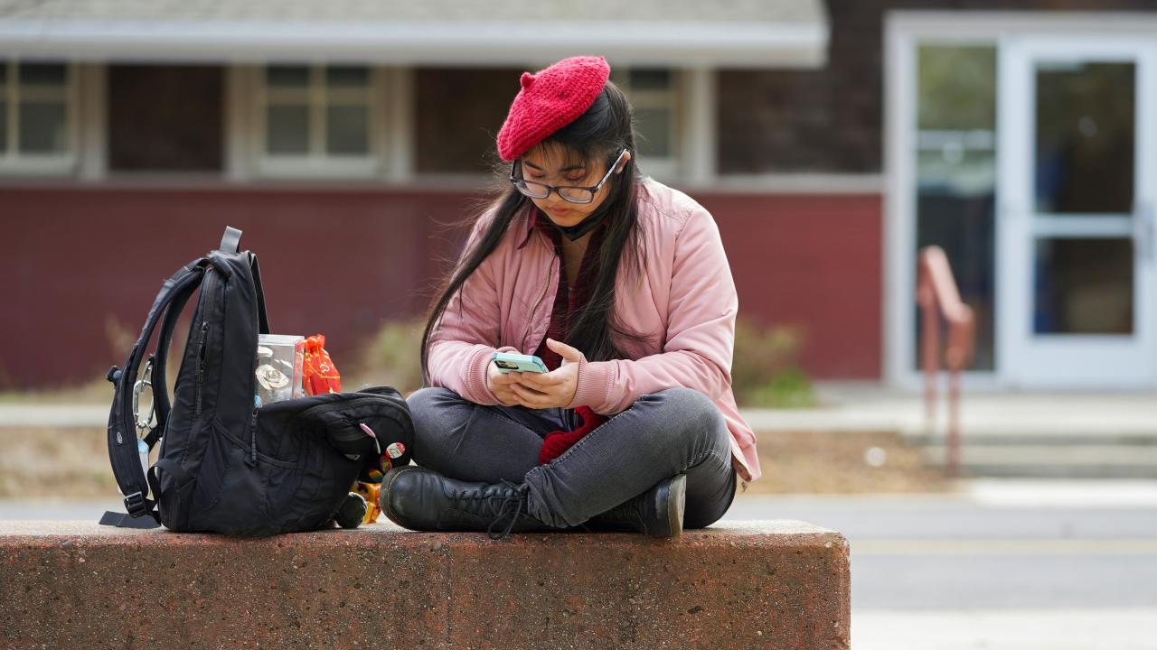 A student wearing a beret uses their smartphone outside of the UC Davis Craft Center.