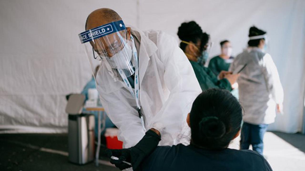 UC President Michael V. Drake, in lab coat, administers a vaccination.