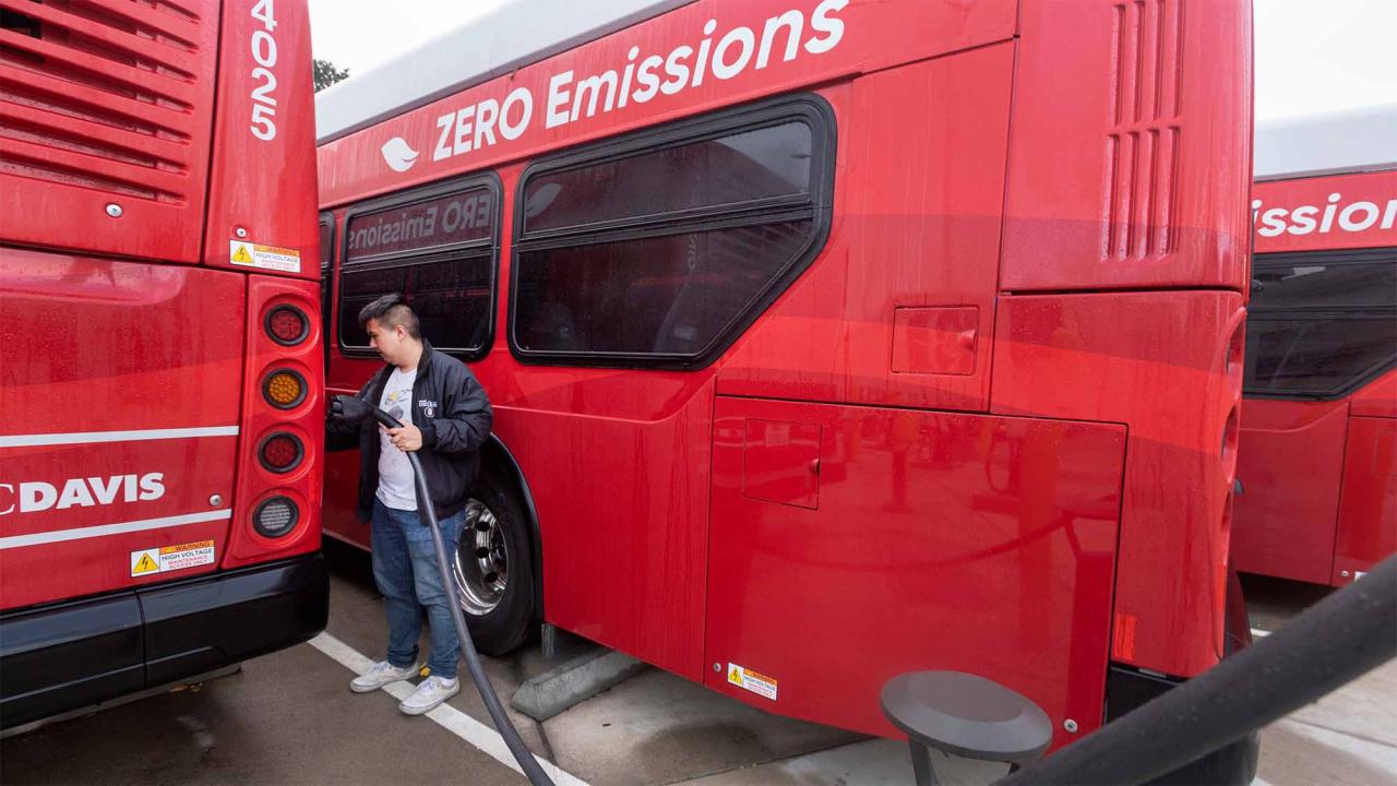 Person plugs red Unitrans bus into electric charger