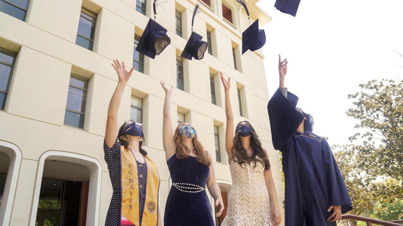 Students wearing face coverings toss their grad caps into the air.