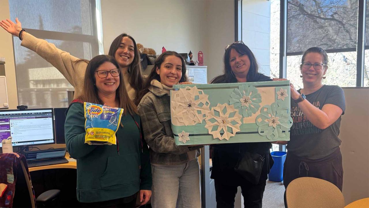 Group of people smile, wave and hold up bag of Tide Pods.