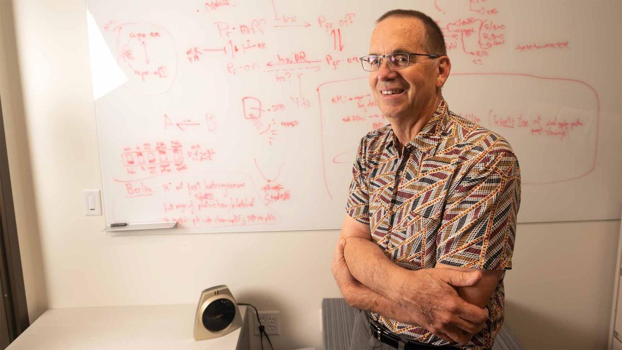 Man stands next to whiteboard, which is covered with writing