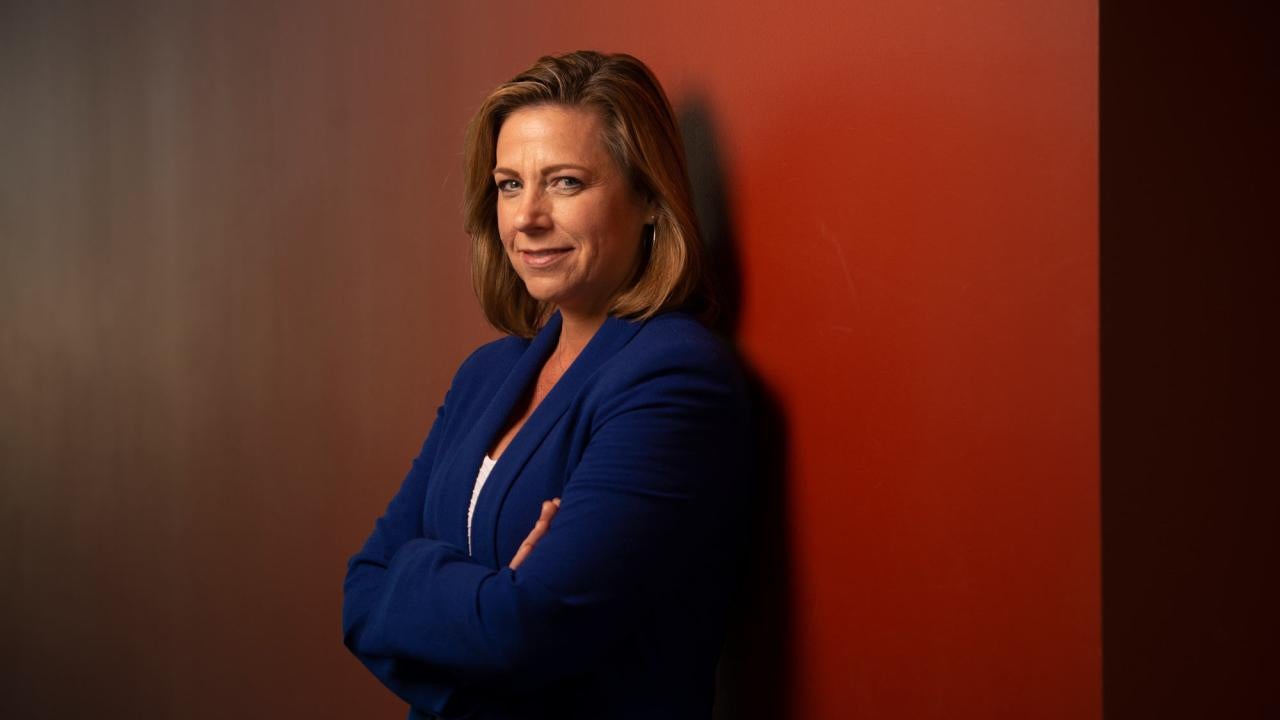 Jonna Mazet portrait, arms folded, standing against red wall