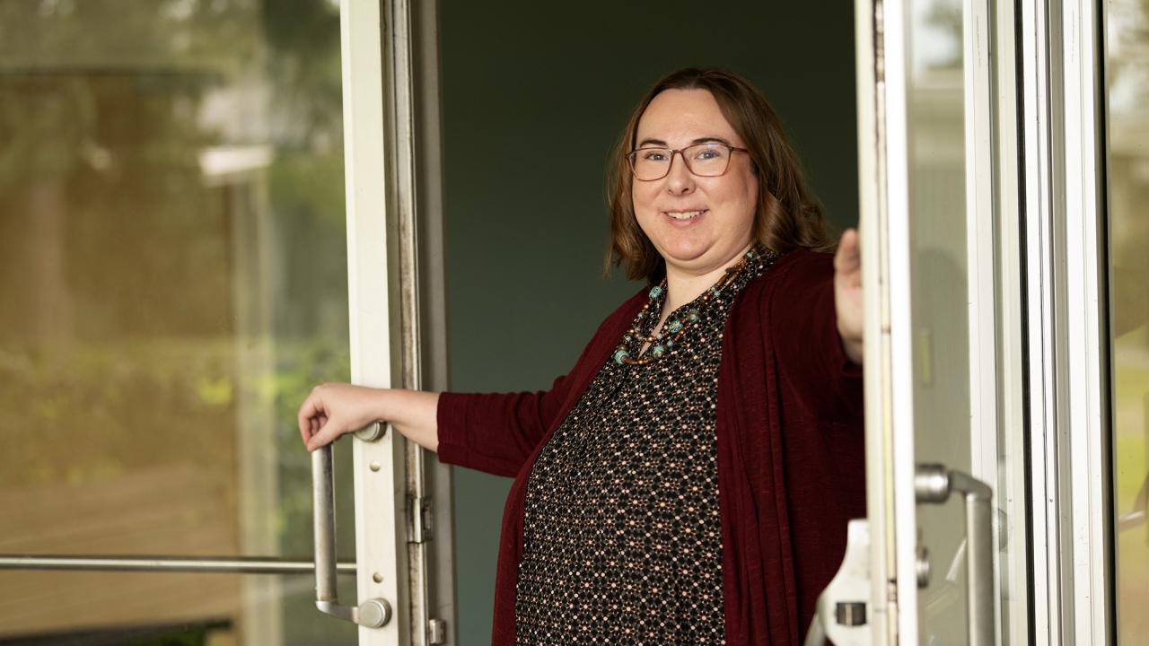 Katie Healey holds open a glass door to a building.