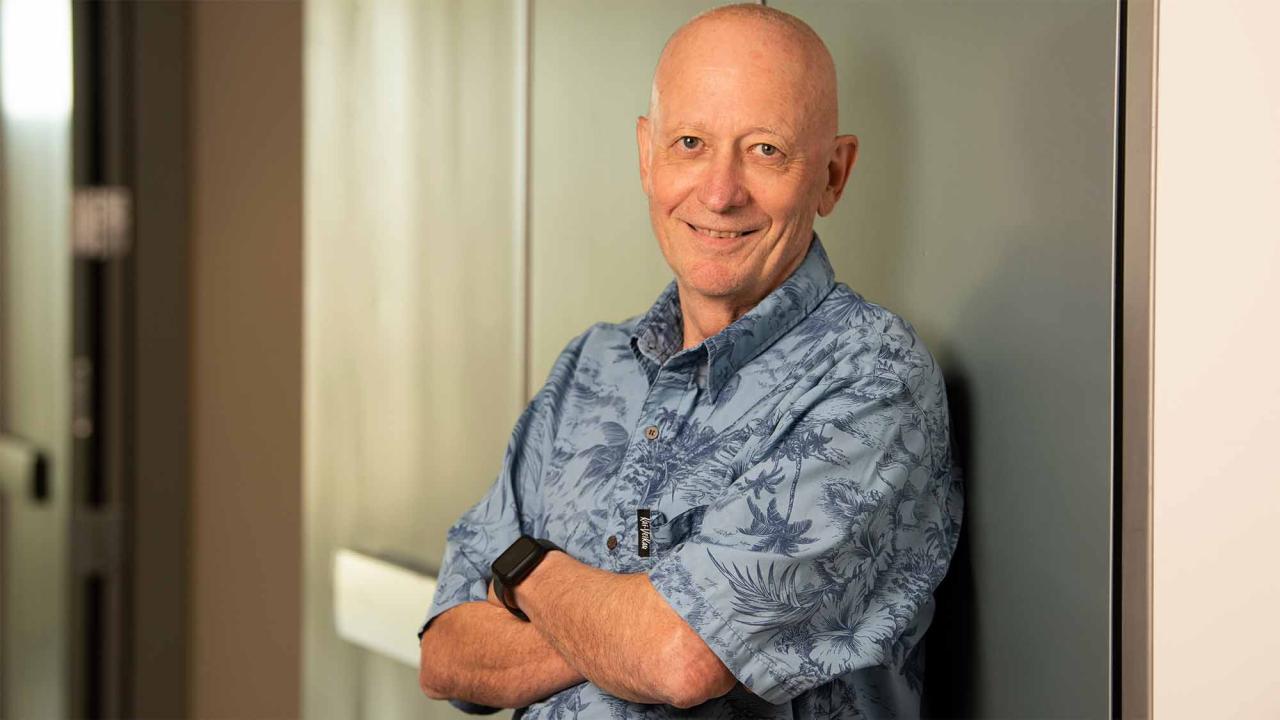 Man with short-sleeved blue shirt poses for photo near wall