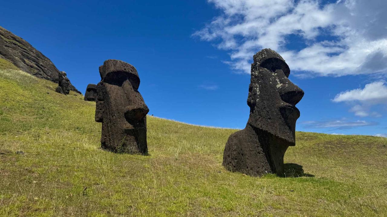 Two massive stone carvings of heads stand on a grassy field under bright blue skies.
