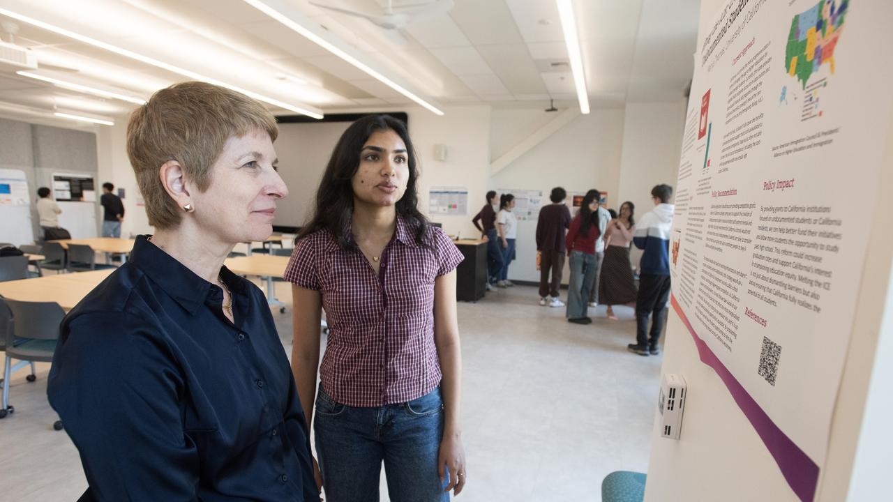 Two women look at a poster with others in the background.