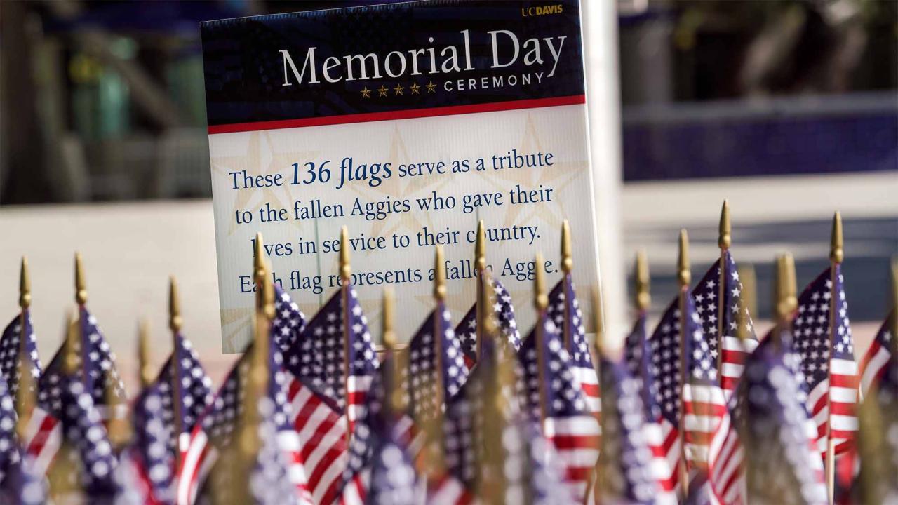 American flags displayed next to a sign that reads UC Davis Memorial Day Ceremony: These 136 flags serve as a tribute to the fallen Aggies who gave their lives in service to their country. Each flag represents a fallen Aggie.