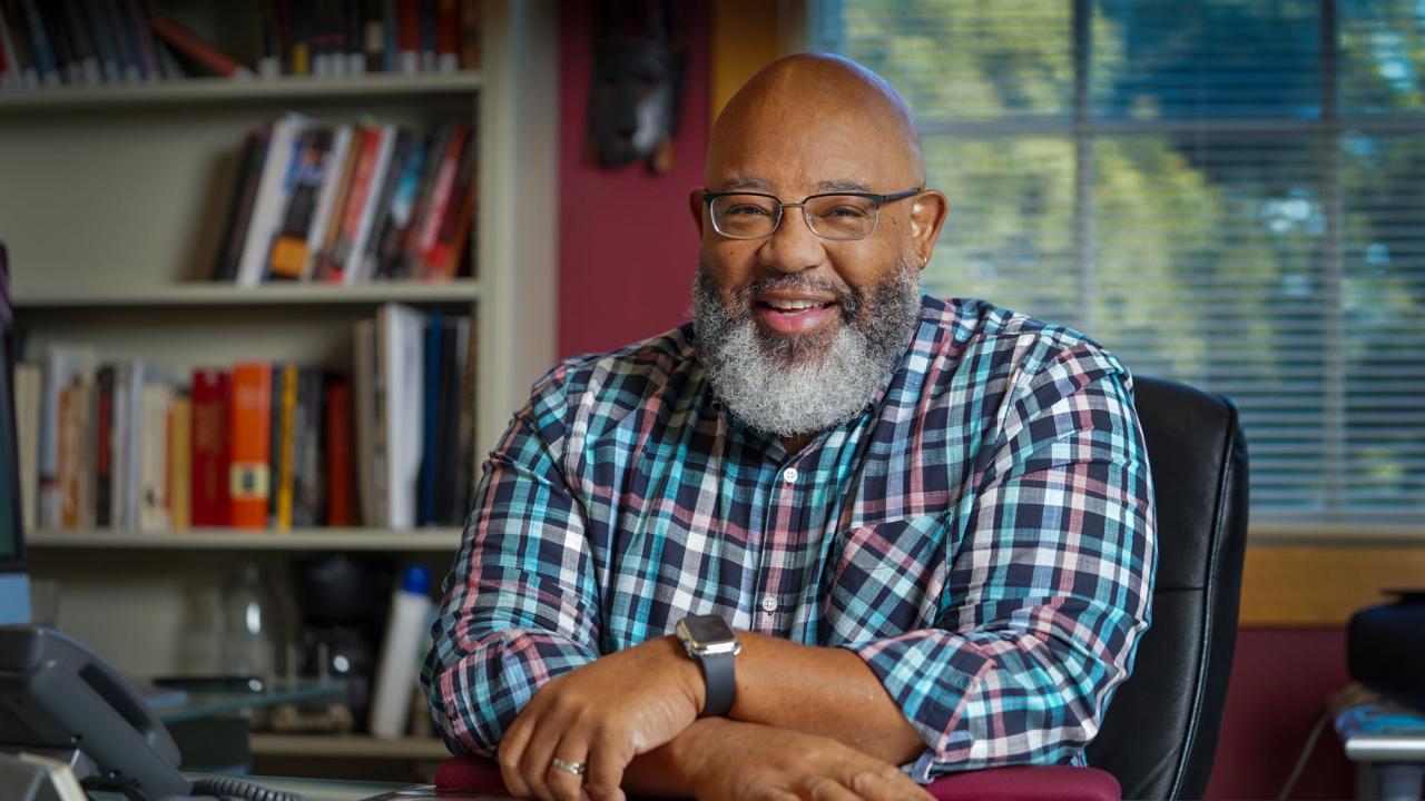 Milmon Harrison, arms folded, at desk