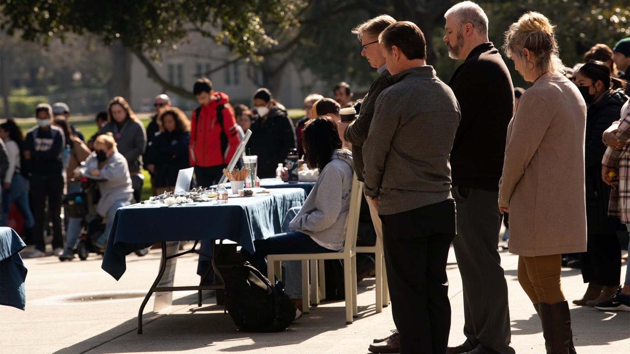 People lower their heads during a moment of silence on the Memorial Union South Patio.