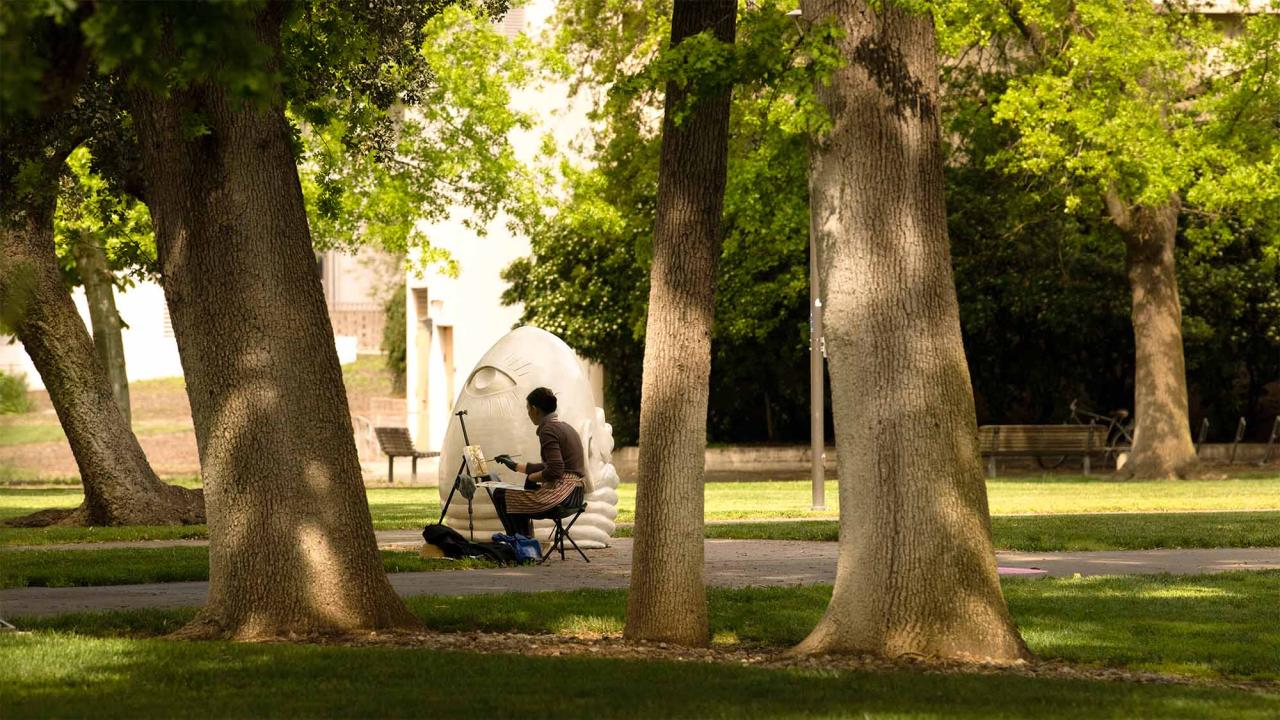 A photograph of a painter working on a canvas while near the statue of the Eye on Mrak sculpture.
