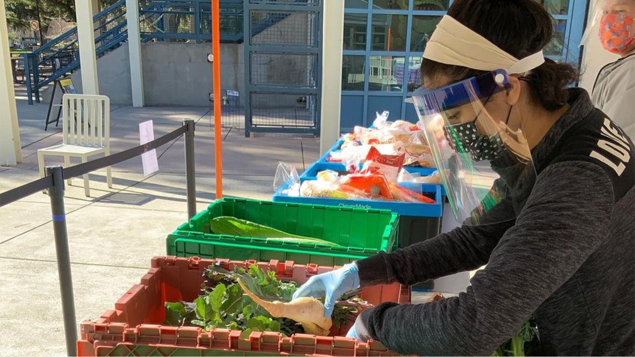 Student wearing face covering pulls vegetables out of large tote.