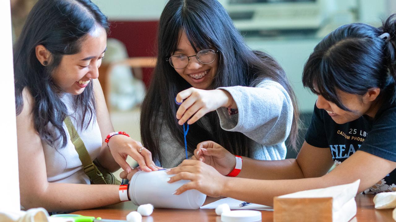 Three students work with cotton balls, a plastic container and string in the annual Engineering Dean's Undergraduate Challenge 