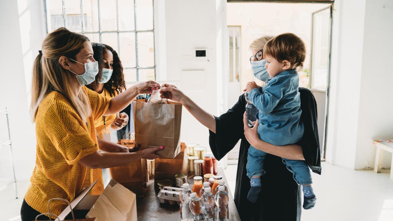 Youth with face coverings giving grocery bag to mother and child