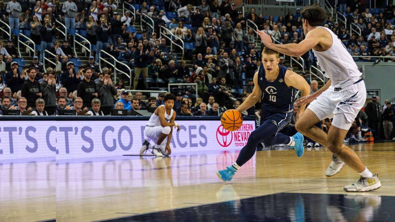 A UC Davis basketball player races across the court, ball in hand, against two players from the University of Nevada, Reno, 