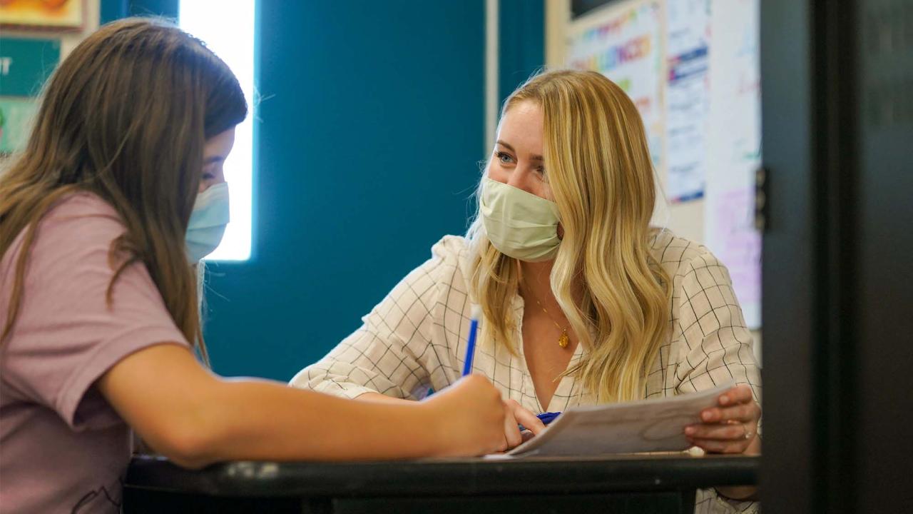 Woman sits at desk with young student.