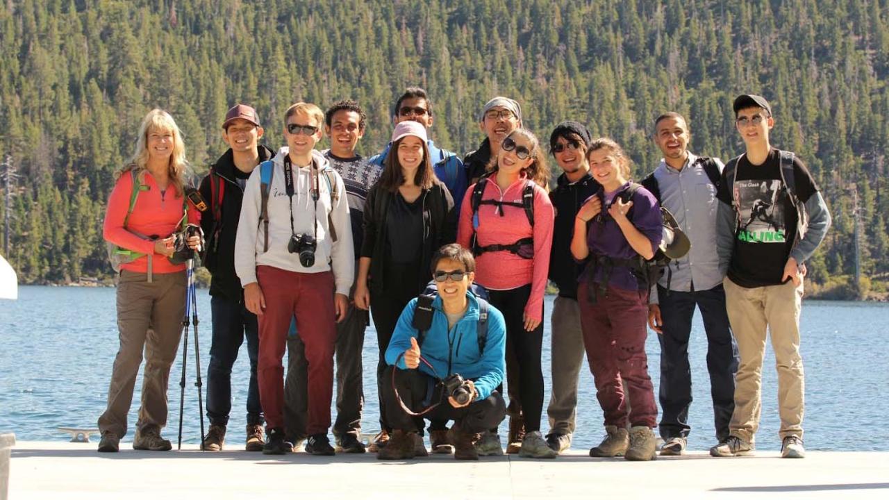 Group of hikers posing together by a lake, surrounded by trees and mountains.