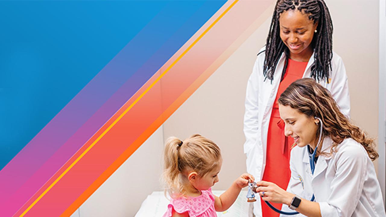 2 people in white lab coats/medical setting, "examining" toy held by girl