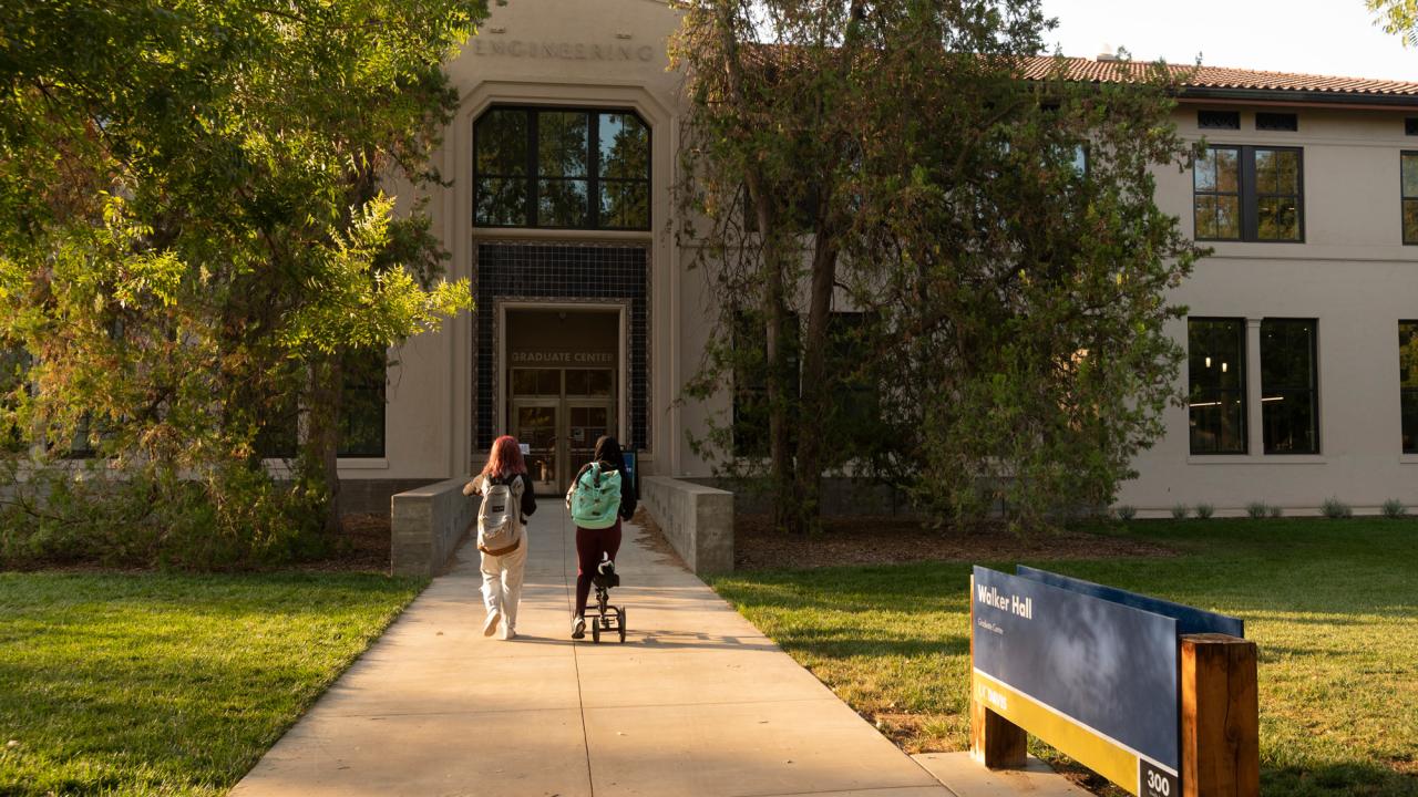 Two women walk toward Walker Hall main entrance.