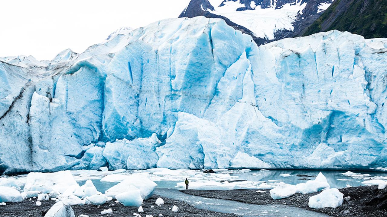 A man stands on the water’s edge at the foot of the massive vertical face of the Spencer Glacier in Alaska. (Getty Images)