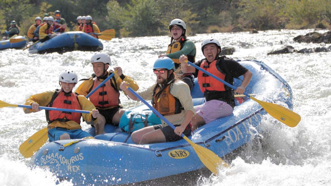 A group of people white-water rafting in a blue inflatable boat.