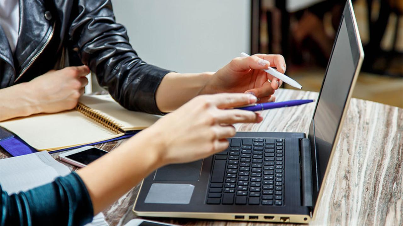Closeup of two people pointing at laptop screen
