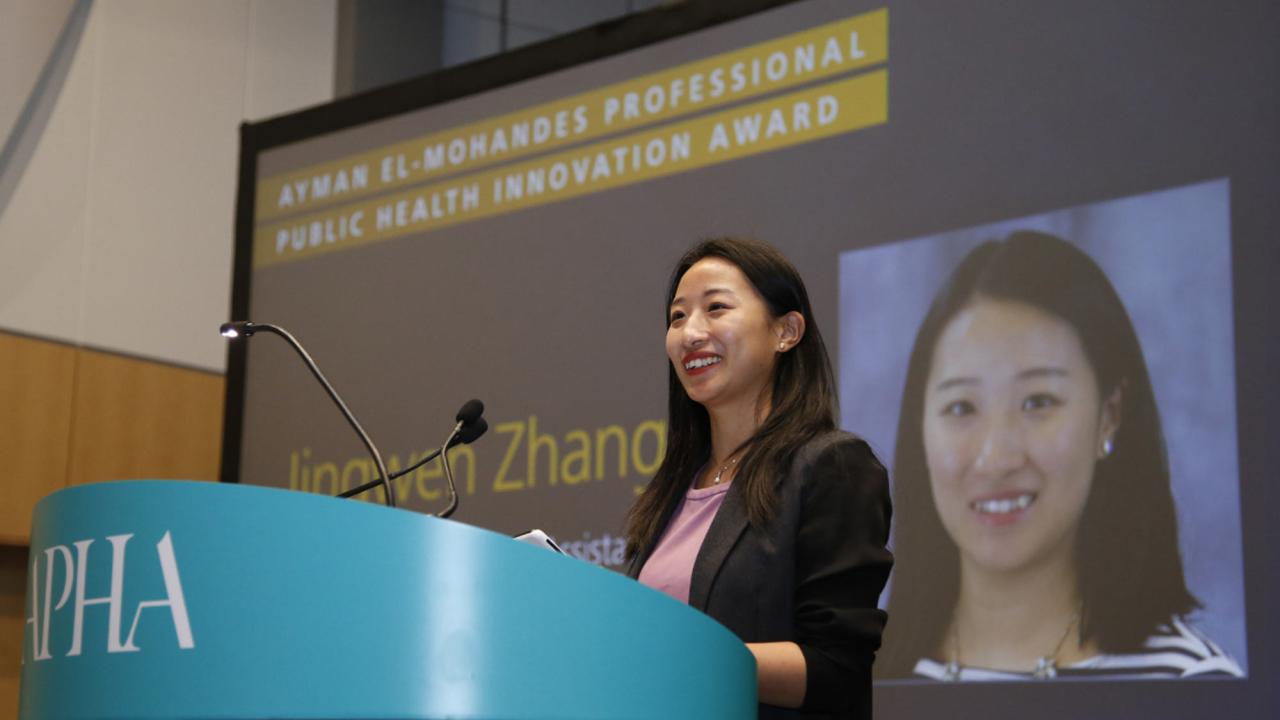 Woman speaks at podium, with her headshot on screen behind her.