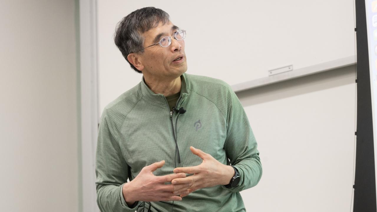 Person wearing green shirt and glasses looks up at whiteboard during lecture