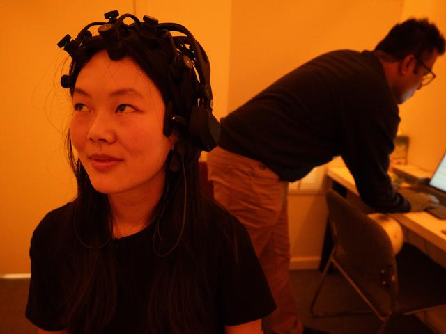 Student sits with EEG equipment on her head in a room lit with amber light