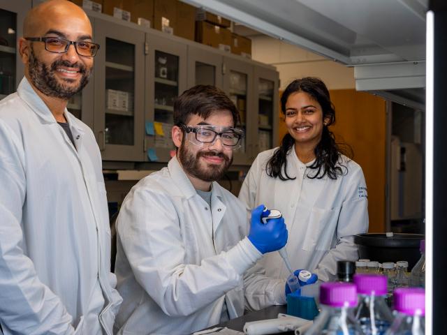 Three researchers in lab coats smile for the camera