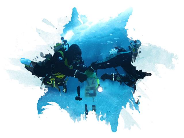 Two divers take samples of the sea floor under a large ice cap