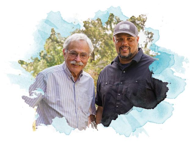Two men pose for a picture in a wooded area