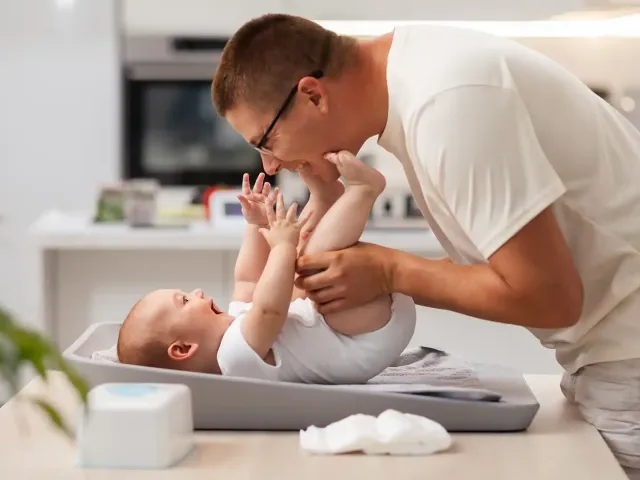 A man leans over to play with his baby before changing a diaper.