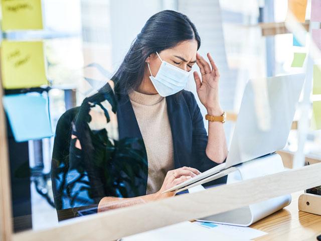 A woman works at her laptop and seems to be struggling with a headache