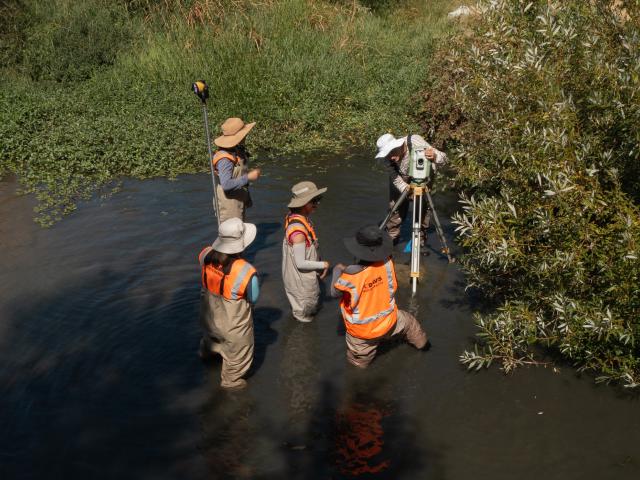 UC Davis researchers photographed from above a creek conduct a stream survey in the water wearing bright orange vests